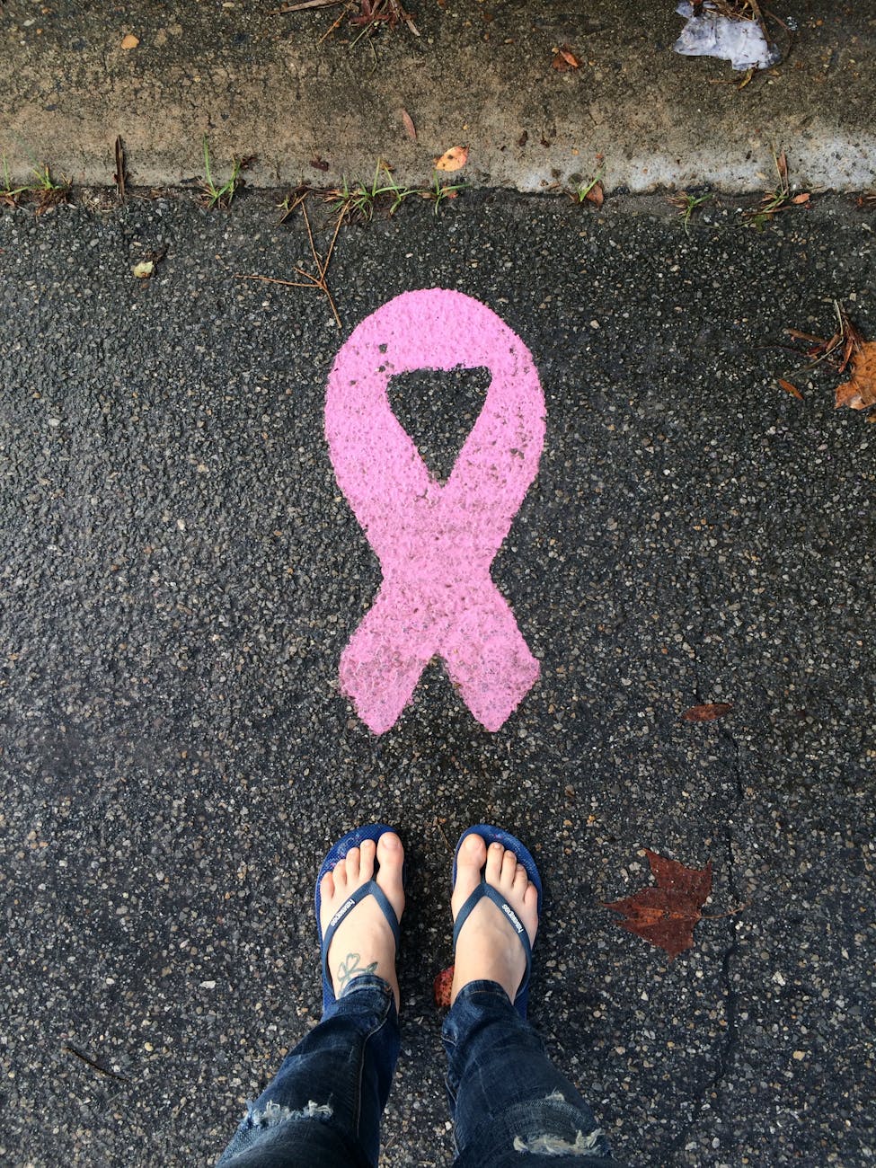 person legs near cancer awareness pink ribbon on asphalt